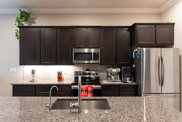 kitchen with sink, dark brown cabinets, stainless steel appliances, light stone countertops, and decorative backsplash