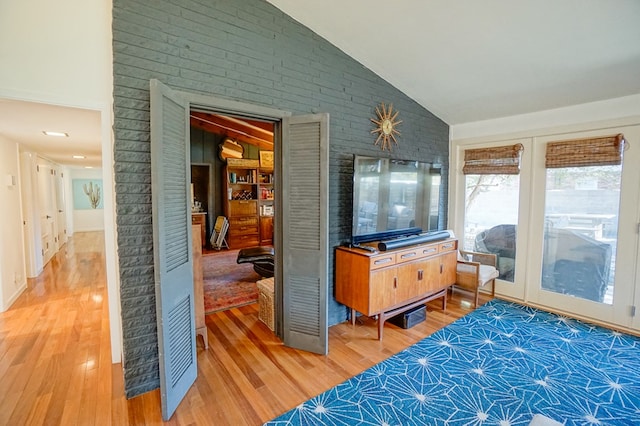 interior space featuring lofted ceiling, hardwood / wood-style flooring, and brick wall