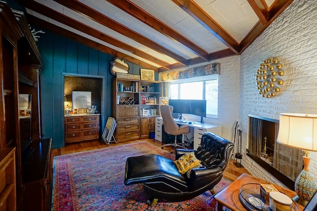 home office featuring vaulted ceiling with beams, hardwood / wood-style flooring, a brick fireplace, and brick wall