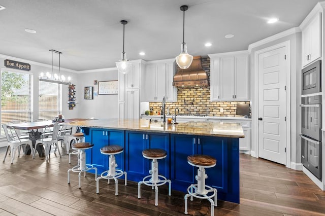 kitchen with a center island with sink, white cabinets, and decorative light fixtures