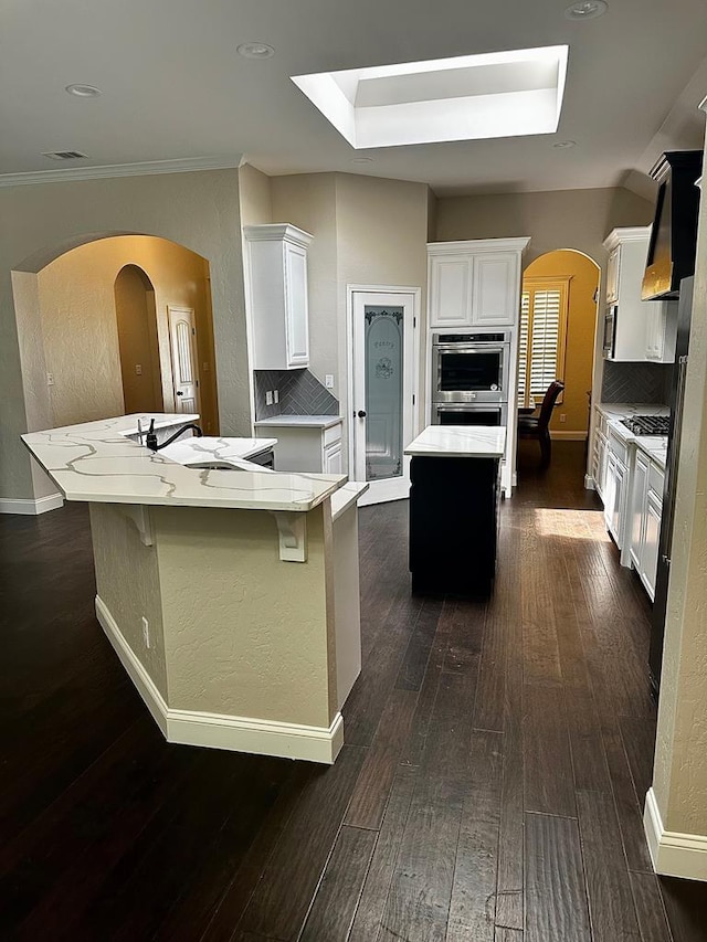 kitchen with stainless steel double oven, arched walkways, a center island, and tasteful backsplash