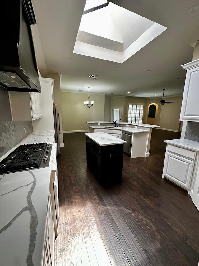 kitchen with exhaust hood, ceiling fan with notable chandelier, dishwasher, a center island, and baseboards