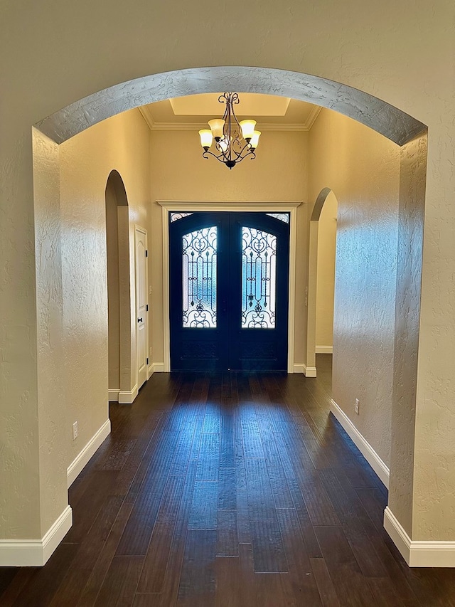 entryway featuring a notable chandelier, crown molding, arched walkways, and a textured wall