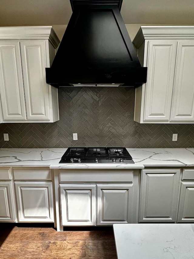 kitchen featuring light stone counters, gas cooktop, ventilation hood, backsplash, and white cabinets