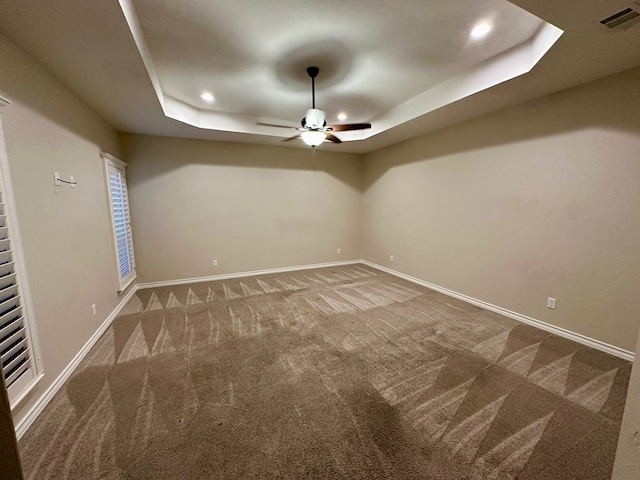 carpeted spare room with baseboards, ceiling fan, a tray ceiling, and visible vents