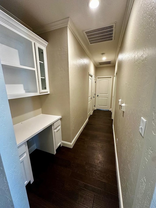 corridor featuring dark wood-style flooring, ornamental molding, visible vents, and a textured wall