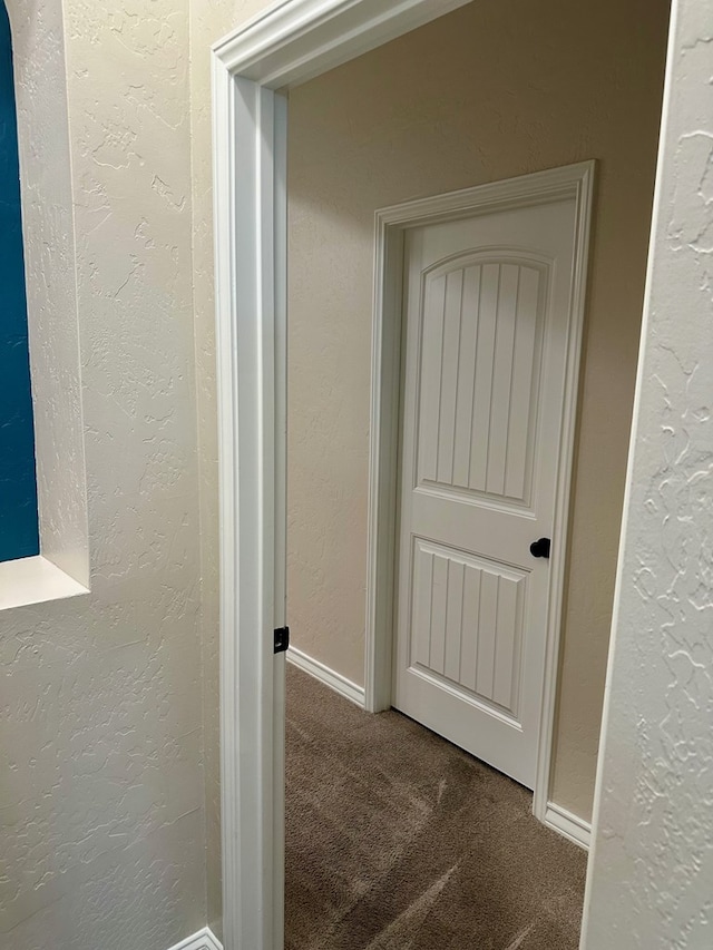 corridor featuring carpet flooring and a textured wall