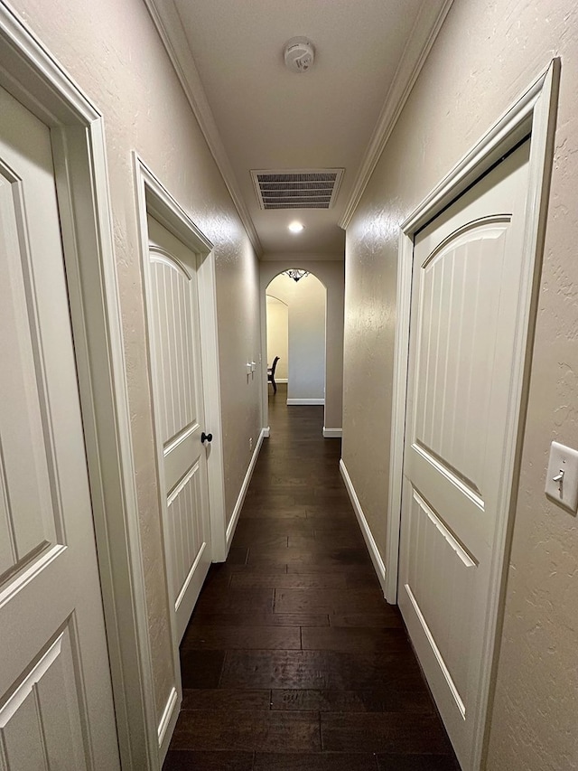 hallway featuring visible vents, dark wood-style flooring, arched walkways, a textured wall, and ornamental molding