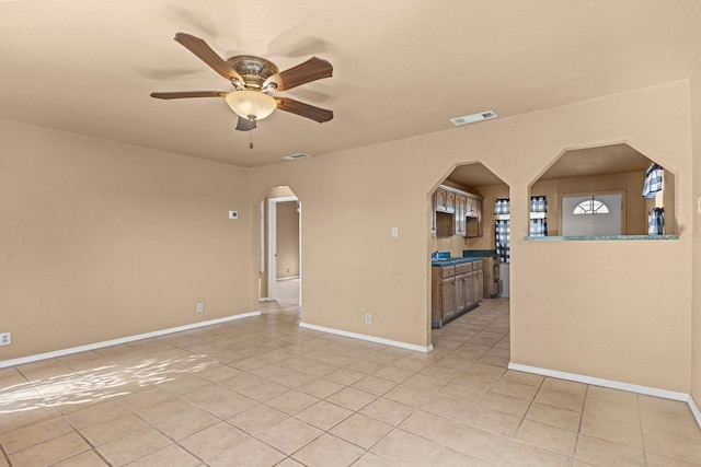spare room with arched walkways, light tile patterned floors, ceiling fan, and baseboards