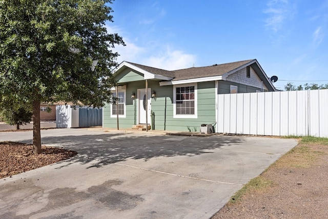 view of front facade with fence, concrete driveway, and a shingled roof