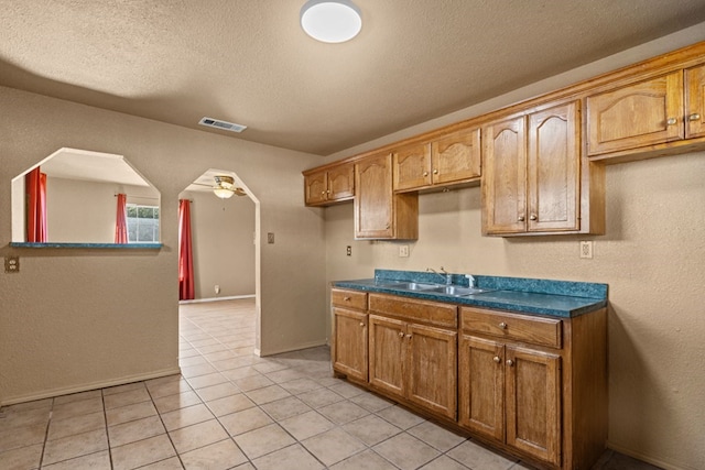kitchen featuring a sink, a textured ceiling, light tile patterned flooring, dark countertops, and baseboards