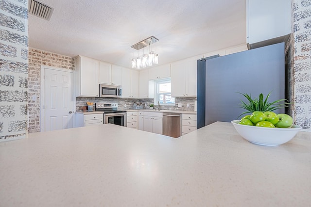 1207 Kansas, Midland, TX 79705 - kitchen featuring appliances with stainless steel finishes, light countertops, white cabinetry, tasteful backsplash, and hanging light fixtures