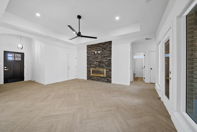 unfurnished living room with a raised ceiling, ceiling fan, a fireplace, and light parquet floors