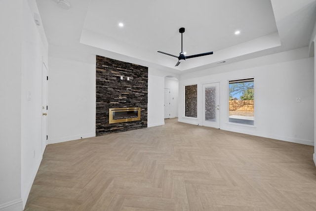 unfurnished living room with a tray ceiling, a stone fireplace, and light parquet flooring