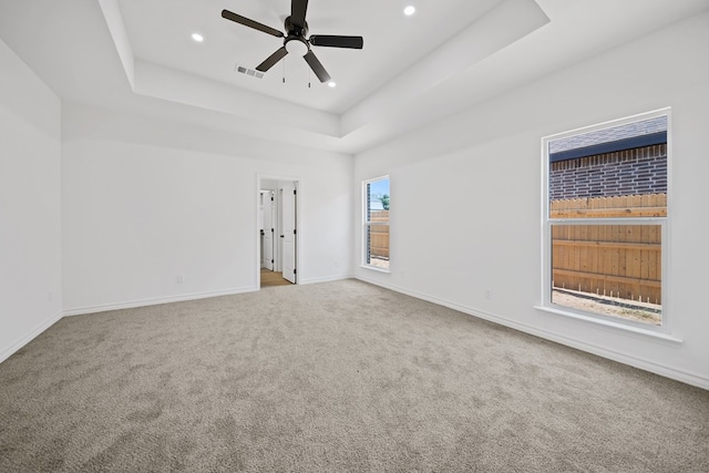 carpeted spare room with a raised ceiling and ceiling fan