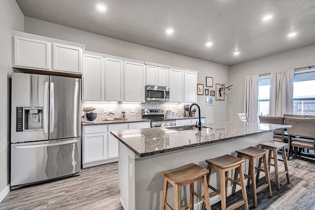 2408 Partridge St, Midland, TX 79705 - kitchen featuring appliances with stainless steel finishes, light wood-style floors, dark stone countertops, white cabinetry, and recessed lighting