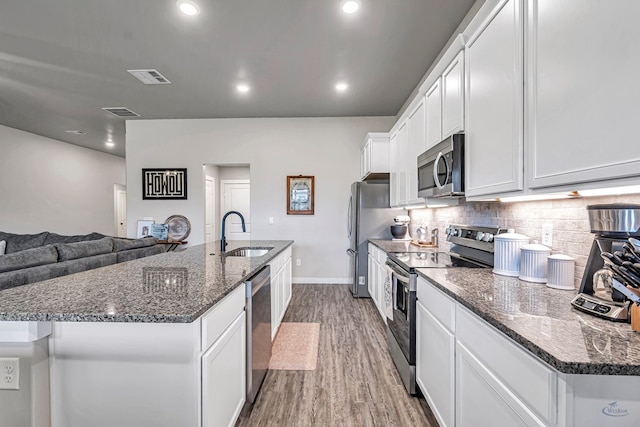 2408 Partridge St, Midland, TX 79705 - kitchen with appliances with stainless steel finishes, a kitchen island with sink, wood finished floors, white cabinets, and backsplash