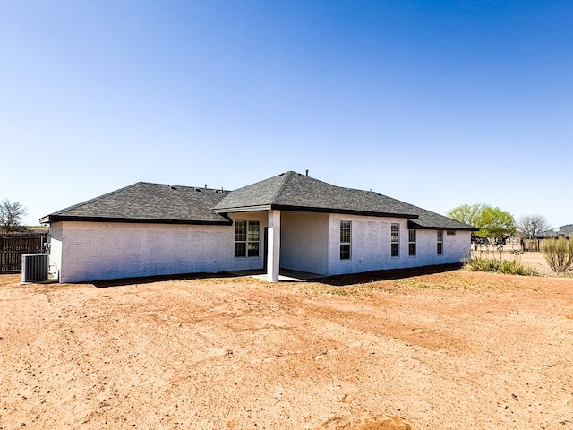 view of front of house with brick siding, central AC unit, a shingled roof, and fence