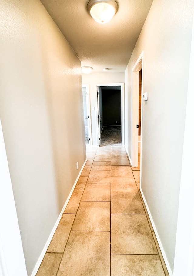 corridor featuring light tile patterned floors, baseboards, and a textured ceiling