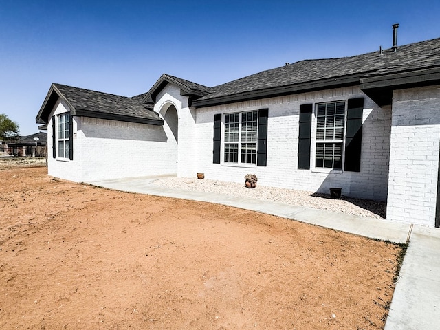 view of property exterior featuring brick siding and roof with shingles