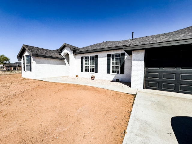 ranch-style house with a garage, brick siding, driveway, and roof with shingles