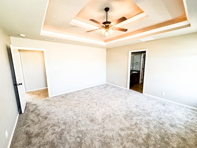 spare room featuring visible vents, a ceiling fan, a tray ceiling, carpet, and baseboards