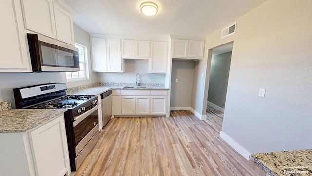 kitchen with baseboards, white cabinets, visible vents, stainless steel appliances, and a sink