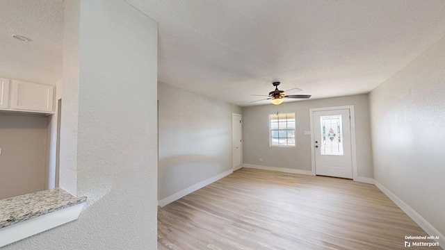 interior space featuring a textured wall, ceiling fan, a textured ceiling, light wood-type flooring, and baseboards