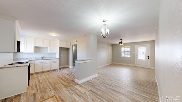 kitchen featuring a textured ceiling, a sink, white cabinetry, baseboards, and light wood-style floors