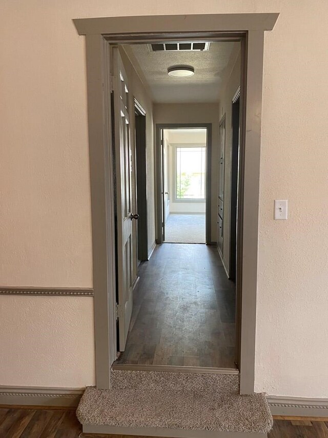 hall with a textured ceiling and dark hardwood / wood-style flooring