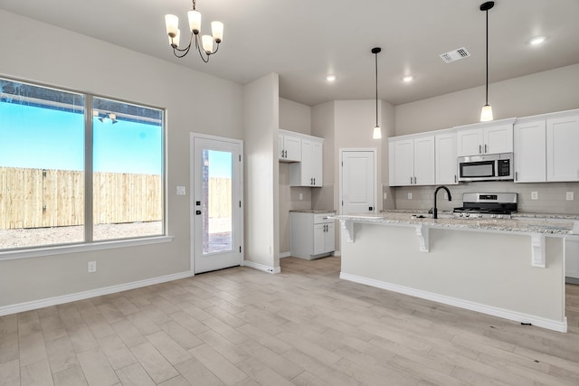 kitchen featuring pendant lighting, a breakfast bar area, appliances with stainless steel finishes, an island with sink, and white cabinets