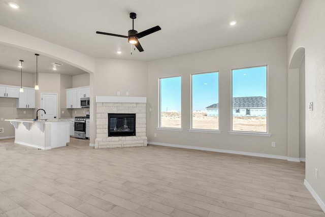 unfurnished living room with a stone fireplace, light wood-type flooring, sink, and ceiling fan