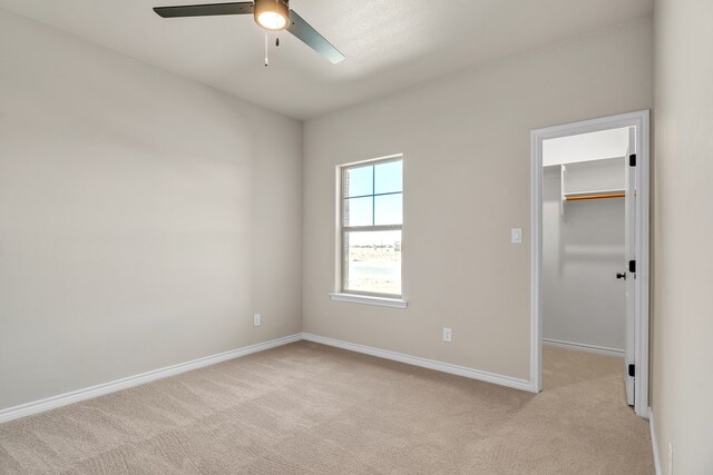 unfurnished bedroom featuring a walk in closet, light carpet, ceiling fan, and a closet