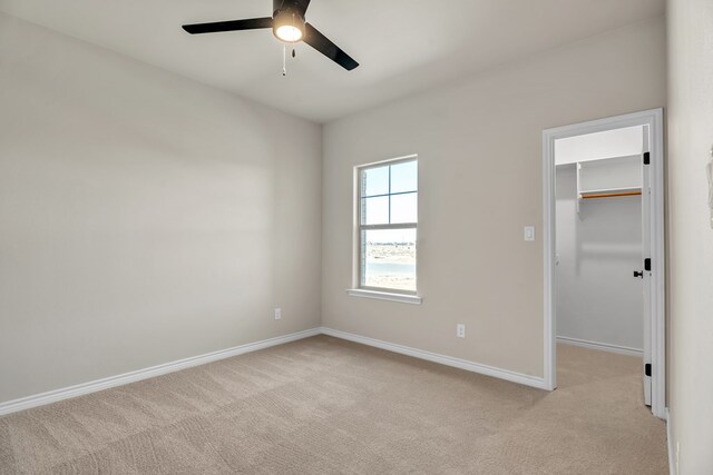 unfurnished bedroom featuring ceiling fan, a closet, a spacious closet, and light carpet