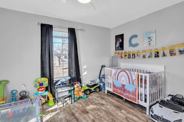 bedroom featuring hardwood / wood-style floors, a crib, and ceiling fan