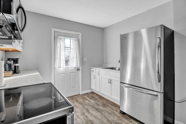 kitchen with sink, light hardwood / wood-style flooring, stainless steel fridge, electric range oven, and white cabinets