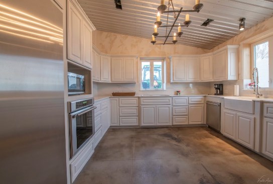 kitchen featuring stainless steel appliances, vaulted ceiling, sink, an inviting chandelier, and white cabinets