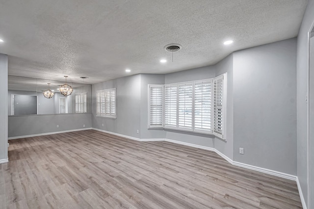 empty room featuring visible vents, baseboards, an inviting chandelier, wood finished floors, and a textured ceiling