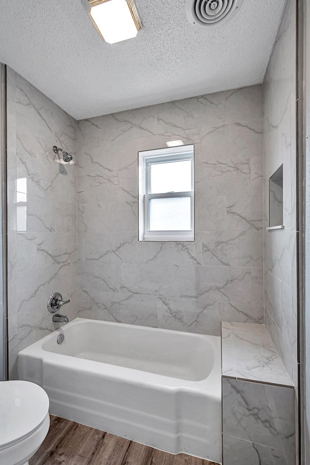 full bath with visible vents, washtub / shower combination, toilet, wood finished floors, and a textured ceiling