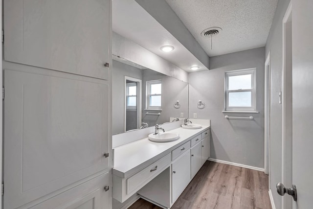 full bathroom featuring visible vents, a sink, a textured ceiling, wood finished floors, and baseboards