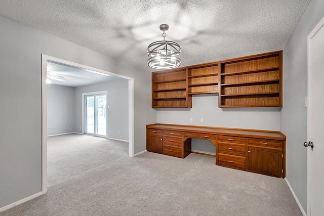 unfurnished office featuring a textured ceiling, light carpet, baseboards, and built in study area