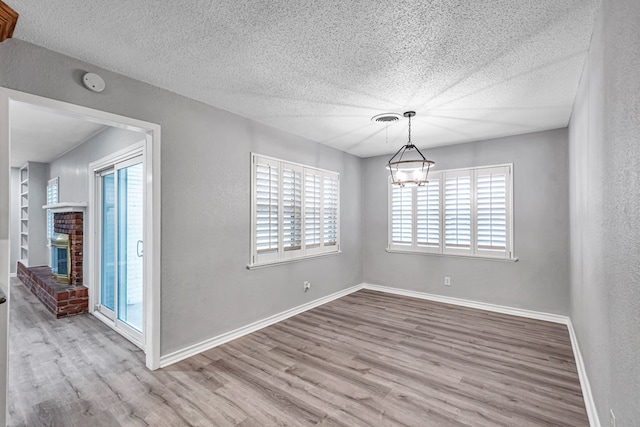 unfurnished dining area with a healthy amount of sunlight, a brick fireplace, baseboards, and wood finished floors