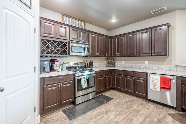 6108 Copper Sky Ct, Midland, TX 79705 - kitchen with appliances with stainless steel finishes, dark brown cabinets, light wood finished floors, and light stone countertops