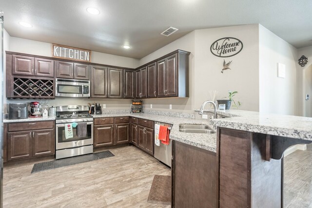 6108 Copper Sky Ct, Midland, TX 79705 - kitchen featuring appliances with stainless steel finishes, a sink, a peninsula, light wood-type flooring, and dark brown cabinetry
