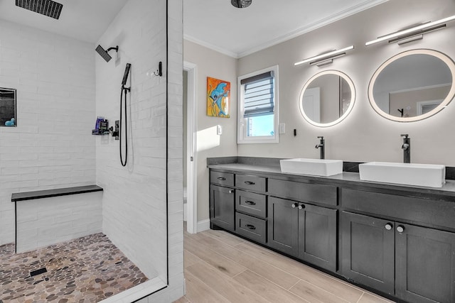 full bathroom with a tile shower, ornamental molding, double vanity, and a sink