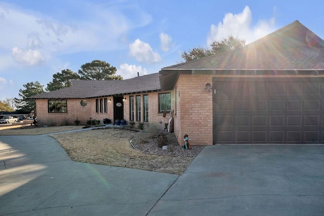 ranch-style home with concrete driveway, an attached garage, brick siding, and a shingled roof