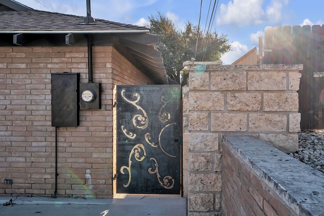 details with brick siding, electric meter, and a shingled roof