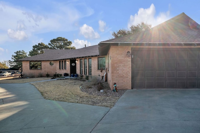 ranch-style house featuring a garage, brick siding, roof with shingles, and driveway