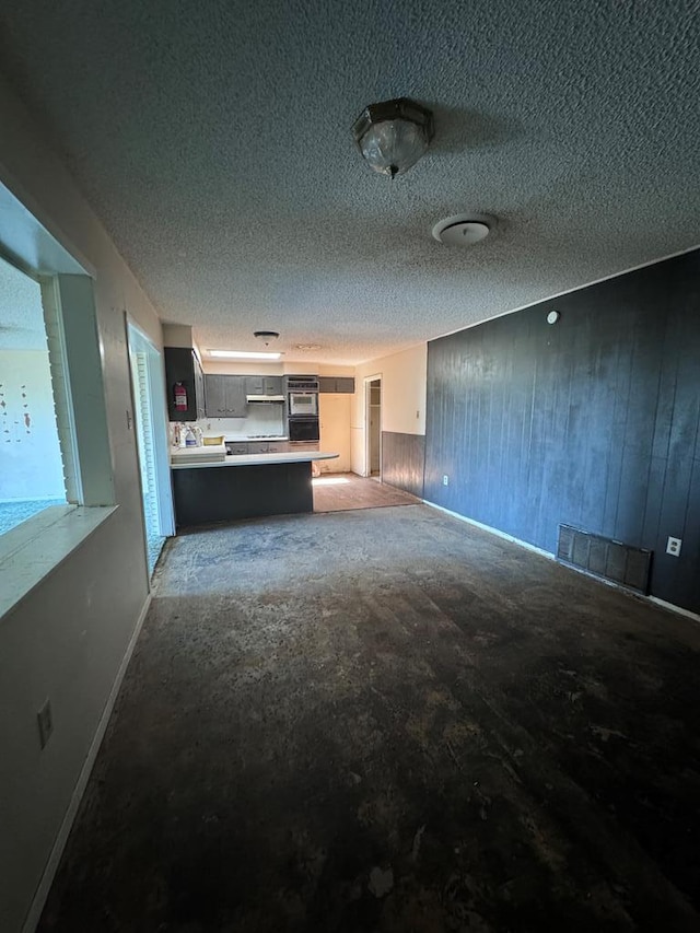 unfurnished living room featuring wooden walls and a textured ceiling