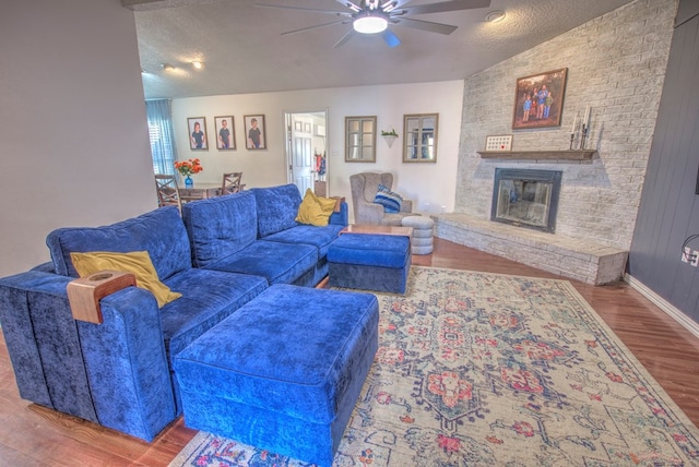 living room with a brick fireplace, wood-type flooring, a textured ceiling, and ceiling fan